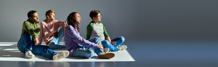 young men in casual wear sitting on floor looking away on grey backdrop, cultural diversity, bannerの写真素材