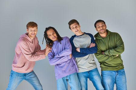four cheerful men in casual outfits smiling at camera posing on grey backdrop, cultural diversityの写真素材