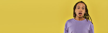 surprised african american man in purple sweatshirt with pierced lip on yellow background, bannerの写真素材