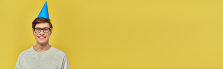 joyful young man in casual simple attire and birthday hat smiling at camera, birthday, bannerの写真素材