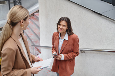 two colleagues standing on stairs looking at each other holding phone and documents, coworkingの写真素材