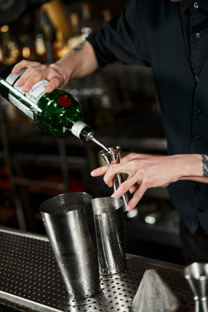cropped view of bartended pouring alcohol drink into jigger while mixing cocktail on bar counterのeditorial素材