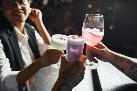 happy african american woman clinking glasses with tattooed men while resting in bar after workの写真素材