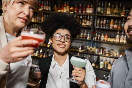 african american woman smiling near multiethnic work friends holding drinks and talking in barの写真素材