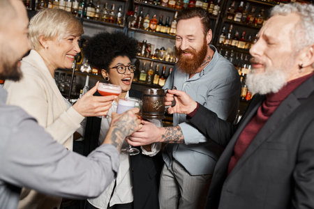 happy multiethnic workmates spending time after work in bar and toasting with alcohol drinksの写真素材