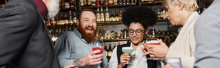excited bearded man laughing near multicultural friends holding glasses with drinks in bar, bannerの写真素材