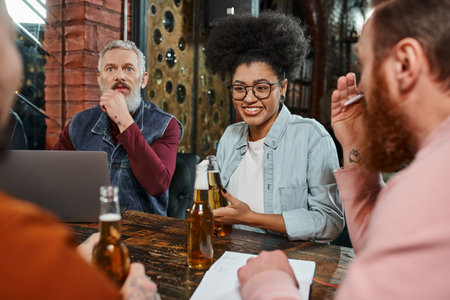 cheerful african american woman talking to multiethnic workmates during discussion on startup in pubの写真素材