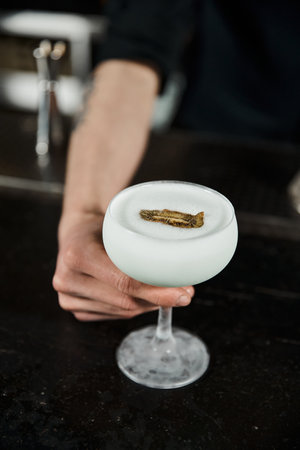 cropped view of bartender presenting glass of milk punch with kiwi slice, cocktail hour in barの写真素材