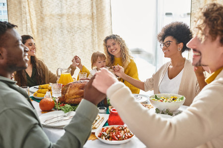 cheerful multiracial friends and family holding hands and praying together at Thanksgiving tableの写真素材