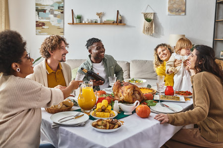african american man pouring wine into glass, multiracial family celebrating Thanksgiving at homeの写真素材