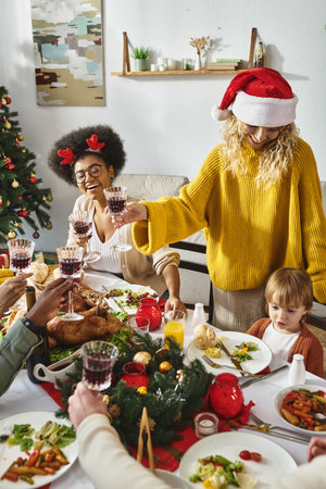 Happy multiethnic friends and family in santa hats cheering glasses while celebrating Christmasの写真素材