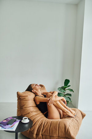attractive barefoot woman resting on bean bag chair near coffee table with cup of black coffeeの写真素材