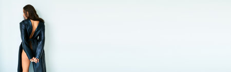 banner of brunette woman in leather coat and lace panties standing near grey wall, sexy legsの写真素材