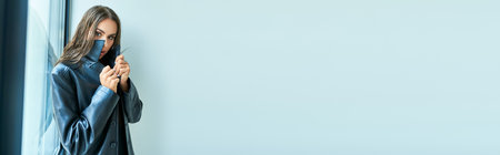 banner of sexy woman with brunette wet hair and blue eyes posing in black leather coat near windowの写真素材