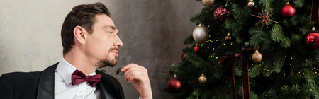 well-dressed gentleman with beard wearing tuxedo with bow tie looking at Christmas tree, bannerの写真素材