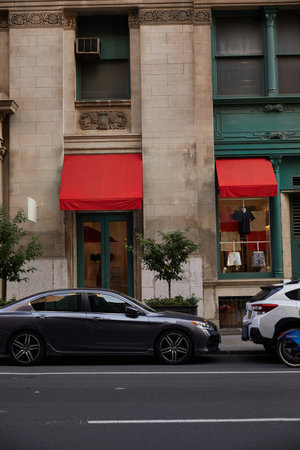 cars parked near vintage building with clothing store and red awnings in downtown of new york city