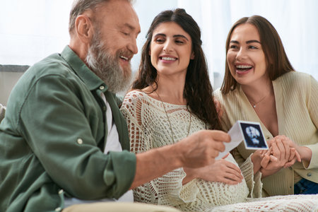 cheerful father smiling with his daughter's partner looking at ultrasound of their baby, ivf concept