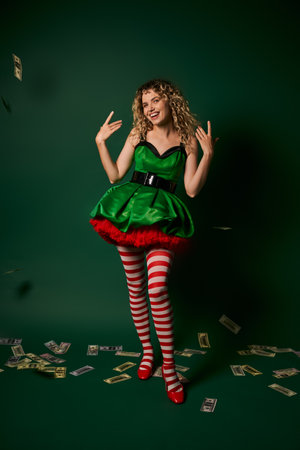 smiley new year elf in green dress and stockings gesturing and smiling with cash on green floor