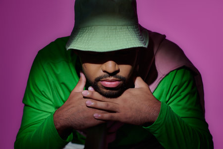 handsome trendy man in green sweatshirt and panama putting his head on hands, fashion concept