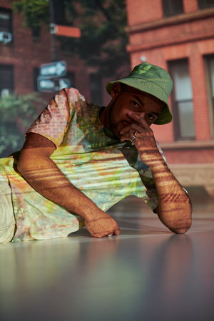 good looking man half lying on floor in stylish outfit in digital projector lights, fashion concept