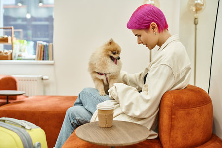 smiling purple-haired woman cuddling cute pomeranian spitz near coffee to go in lounge of dog hotelの写真素材