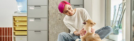 smiling purple-haired pet sitter cuddling fluffy pomeranian spitz in welcoming pet hotel, bannerの写真素材