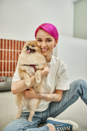 purple-haired woman sitting on floor and embracing pomeranian spitz, affection of dog and pet sitterの写真素材