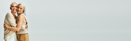 fashionable senior women in trendy casual attire embracing on grey, graceful aging, bannerの写真素材