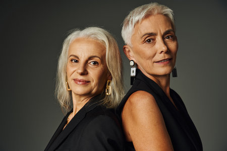 ageless beauty, portrait of elegant senior models with silver hair looking at camera on greyの写真素材