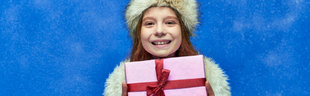 winter holiday banner, happy girl in faux fur jacket and hat holding wrapped gift box on turquoise