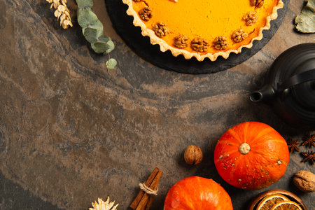 pumpkin pie with walnuts near ripe pumpkins, spices and teapot on stone table, thanksgiving settingの写真素材