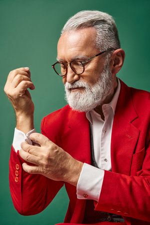portrait of elegant Santa with beard and glasses fastening button on his sleeve, winter conceptの写真素材