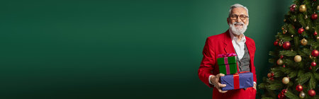 jolly classy Santa with glasses holding pile of gifts next to decorated tree, winter concept, bannerの写真素材