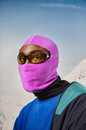 young african american man in pink balaclava and sunglasses looking at camera, winter conceptの写真素材