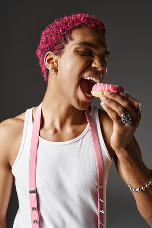 portrait of young pink haired man with pink suspenders eating pink tasty donut, fashion and styleの写真素材