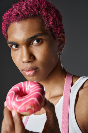portrait of young african american man with pink hair posing with pink donut, fashion and styleの写真素材