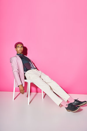 young handsome man in pink blazer with white pants sitting on chair on pink backdrop, doll likeの写真素材