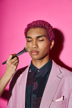 handsome man with curly pink hair posing with closed eyes, hand with makeup brush, doll likeの写真素材