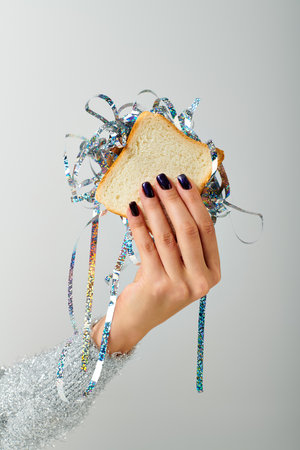 cropped female hand holding sandwich with shiny tinsel on grey backdrop, Happy New Year conceptの写真素材