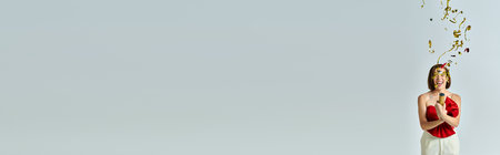 New Year banner, excited young woman in trendy attire clapping festive confetti on grey backdropの写真素材