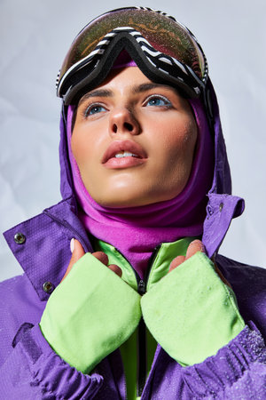 cold weather, dreamy woman in balaclava and ski googles posing in purple winter jacket on greyの写真素材