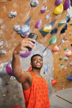 vertical shot of young african american man t taking selfie with rock climbing wall backgroundの写真素材