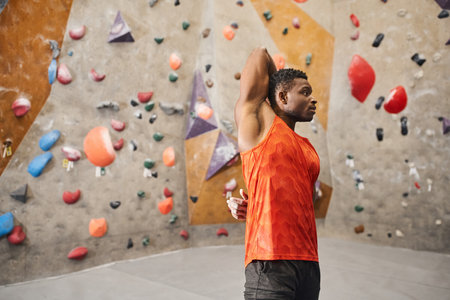 african american athletic man in orange shirt warming up with hands behind back, climbing concept