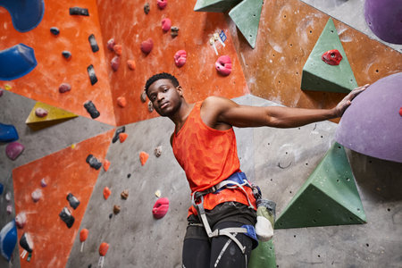 athletic african american male model with alpine harness posing next to rock climbing wallの写真素材