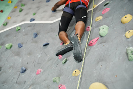 cropped view of legs of strong african american man climbing up bouldering wall with alpine harnessの写真素材