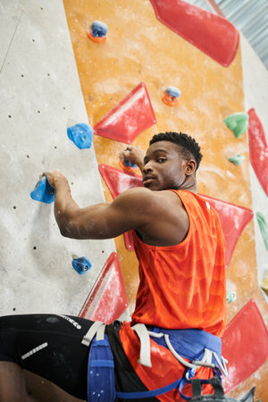 vertical shot of handsome african american man with alpine harness climbing and looking at cameraの写真素材