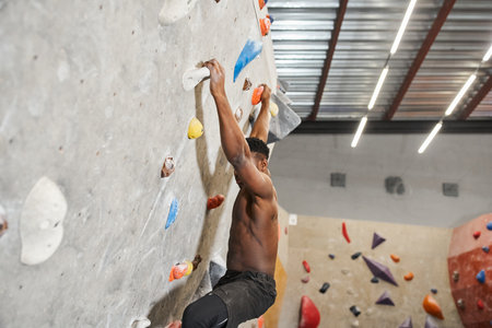 muscular fit african american man with his shirt off climbing up rock wall and looking downの写真素材