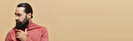 serious and handsome man with beard posing in pink turtleneck jumper  on beige background, banner