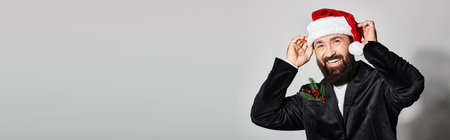 portrait of cheerful handsome man in suit wearing santa hat on grey backdrop, Christmas bannerの写真素材
