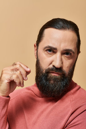 handsome serious man with beard posing in pink turtleneck jumper on beige background, portraitの写真素材